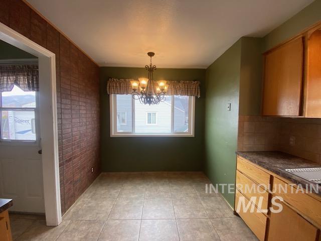 unfurnished dining area featuring light tile patterned floors, brick wall, and a notable chandelier