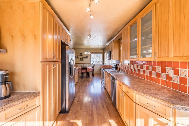 kitchen with stainless steel appliances, a sink, light wood-style floors, decorative backsplash, and glass insert cabinets