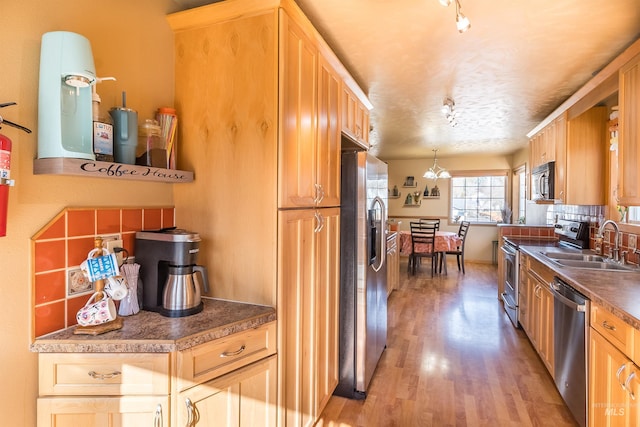 kitchen featuring stainless steel appliances, tasteful backsplash, hanging light fixtures, light wood-style floors, and a sink