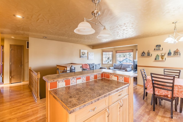 kitchen featuring open floor plan, a center island, light wood-style floors, pendant lighting, and a notable chandelier