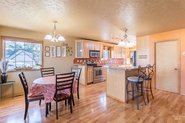 kitchen featuring a breakfast bar, tasteful backsplash, appliances with stainless steel finishes, light wood-style floors, and glass insert cabinets