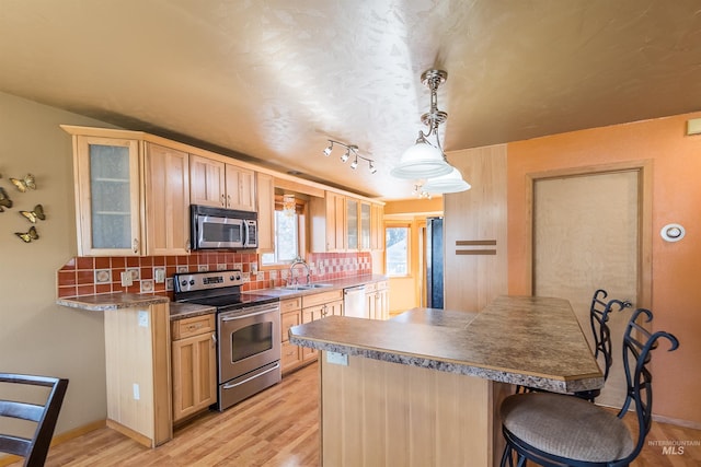 kitchen with a breakfast bar area, light wood finished floors, stainless steel appliances, backsplash, and a sink