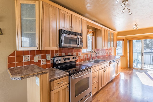 kitchen featuring light brown cabinets, stainless steel appliances, a sink, light wood-type flooring, and tasteful backsplash