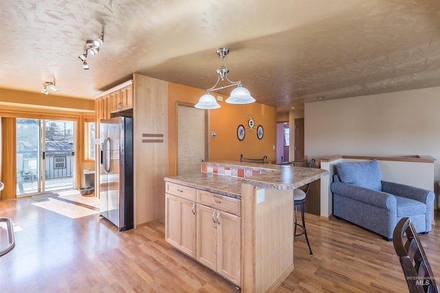 kitchen featuring stainless steel refrigerator with ice dispenser, light wood finished floors, open floor plan, light brown cabinets, and a kitchen breakfast bar