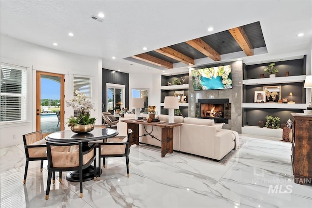 living room featuring a large fireplace, built in shelves, and beamed ceiling