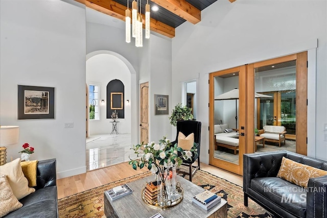 living room with a high ceiling, an inviting chandelier, wood-type flooring, and beam ceiling