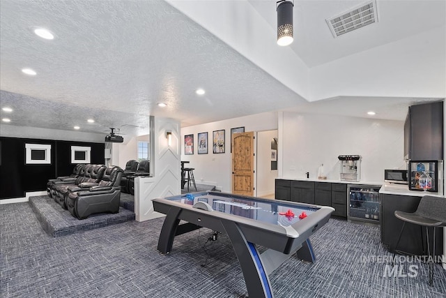 playroom featuring a textured ceiling, bar, wine cooler, and dark colored carpet