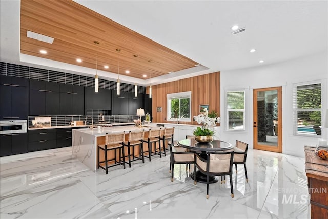 kitchen featuring wooden ceiling, a raised ceiling, a breakfast bar area, white oven, and an island with sink