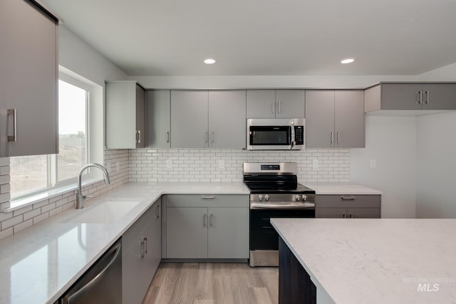 kitchen with light stone countertops, light wood finished floors, a sink, appliances with stainless steel finishes, and gray cabinets