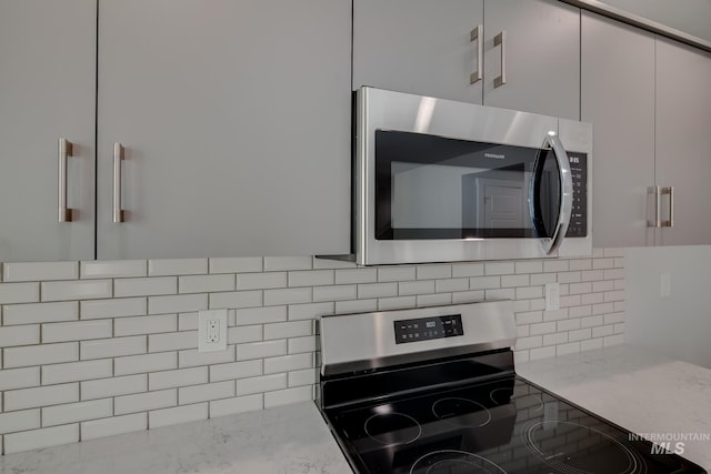 kitchen with backsplash, light stone counters, and appliances with stainless steel finishes
