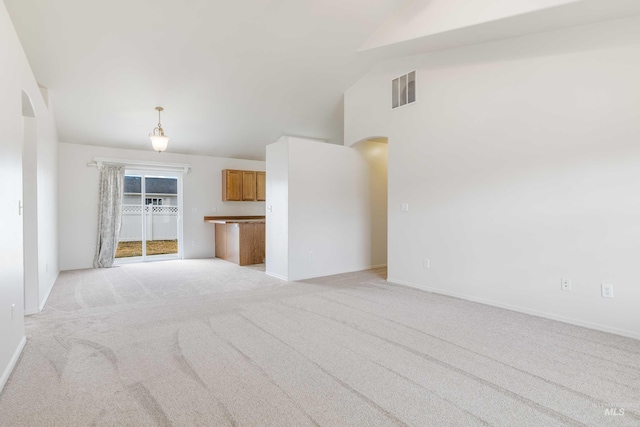 unfurnished living room featuring arched walkways, light colored carpet, visible vents, vaulted ceiling, and baseboards