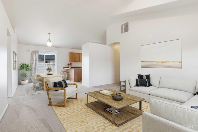 living area with arched walkways, high vaulted ceiling, light carpet, and visible vents