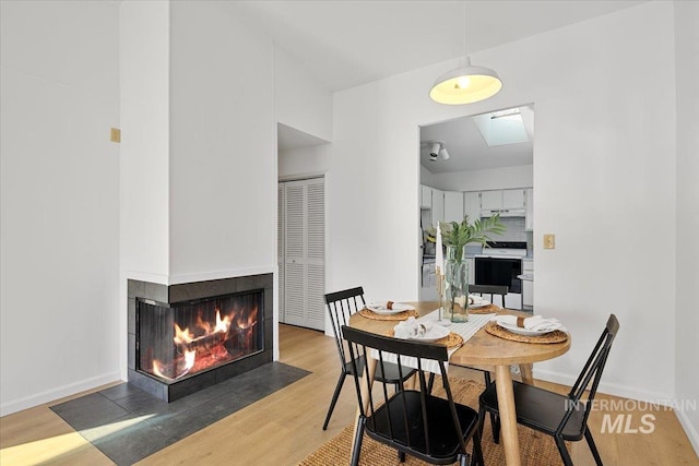 dining room with baseboards, a multi sided fireplace, and wood finished floors