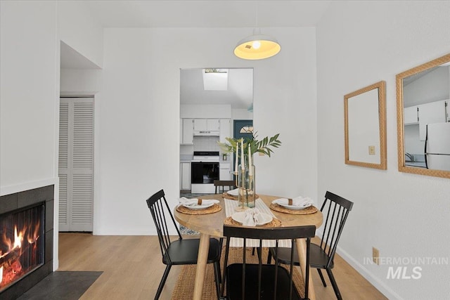 dining area with a fireplace with flush hearth, light wood-type flooring, and baseboards