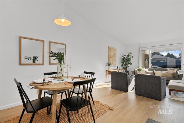 dining room with high vaulted ceiling, light wood-type flooring, and baseboards