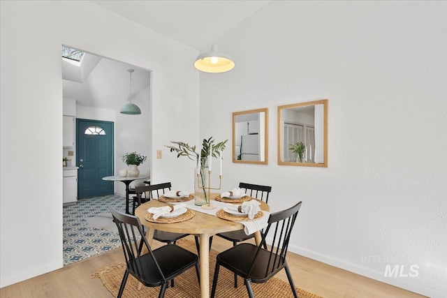 dining room featuring baseboards, light wood-type flooring, and high vaulted ceiling