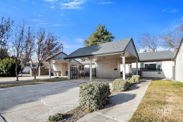 view of front facade with fence, a carport, concrete driveway, and a shingled roof