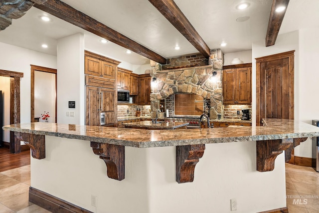 kitchen featuring a breakfast bar area, paneled fridge, beam ceiling, and tasteful backsplash