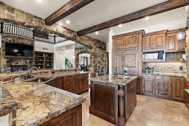 kitchen with a spacious island, beam ceiling, black microwave, sink, and light stone counters