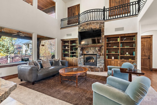 living room featuring a stone fireplace, wood-type flooring, and a towering ceiling