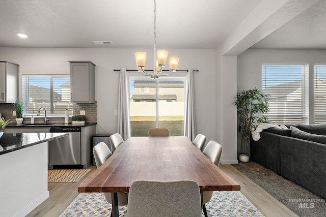 dining room featuring a healthy amount of sunlight, light hardwood / wood-style flooring, an inviting chandelier, and sink