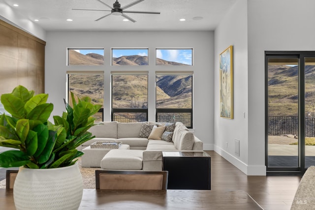 living area with a ceiling fan, plenty of natural light, baseboards, and wood finished floors