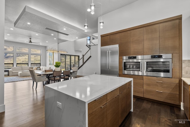 kitchen featuring brown cabinetry, modern cabinets, open floor plan, dark wood-style flooring, and stainless steel appliances