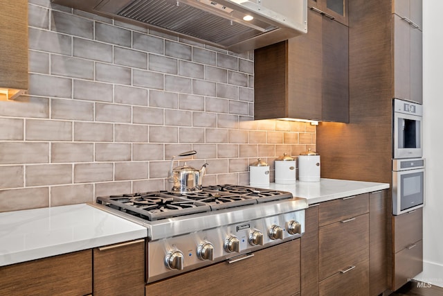 kitchen with premium range hood, appliances with stainless steel finishes, brown cabinetry, and light countertops