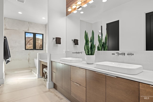 full bath featuring a freestanding bath, double vanity, a sink, and recessed lighting