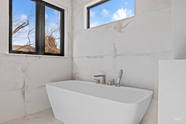 full bath featuring marble finish floor and a freestanding bath