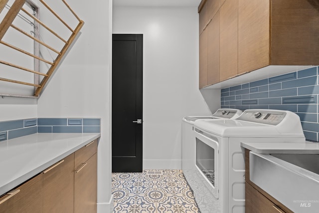 washroom with light tile patterned floors, washing machine and dryer, a sink, baseboards, and cabinet space