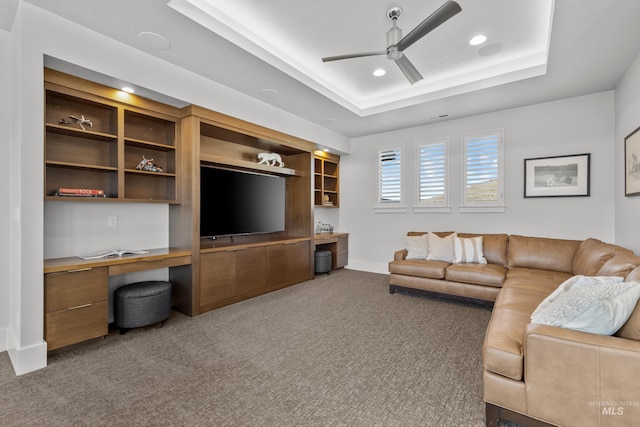 carpeted living area with a tray ceiling, built in desk, recessed lighting, ceiling fan, and baseboards