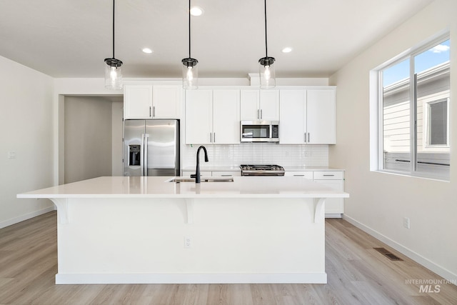 kitchen with a kitchen island with sink, appliances with stainless steel finishes, a sink, and decorative light fixtures