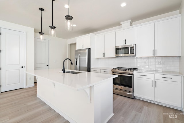 kitchen with appliances with stainless steel finishes, hanging light fixtures, light countertops, white cabinetry, and a sink