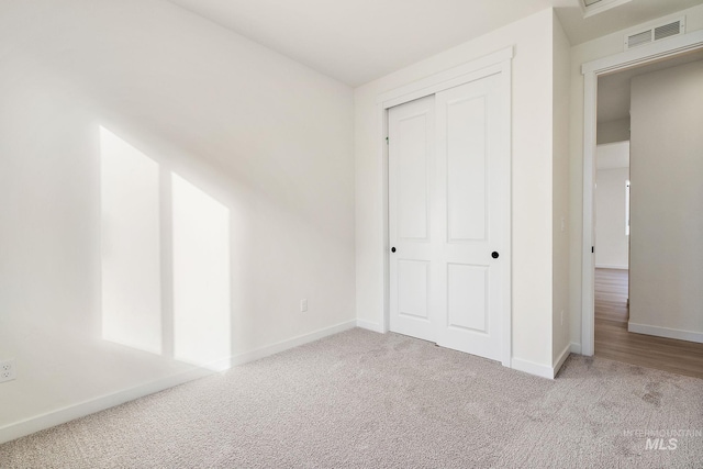 unfurnished bedroom featuring baseboards, visible vents, a closet, and light colored carpet