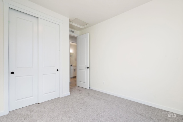 unfurnished bedroom featuring a closet, light colored carpet, visible vents, attic access, and baseboards