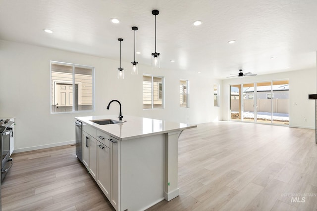 kitchen featuring a center island with sink, light countertops, stainless steel dishwasher, open floor plan, and a sink