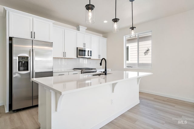 kitchen featuring hanging light fixtures, a center island with sink, stainless steel appliances, and light countertops