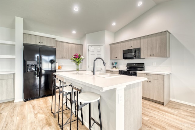 4913 Endicott Dr, Caldwell, ID 83605 - kitchen featuring black appliances, a kitchen bar, a kitchen island with sink, lofted ceiling, and light wood-style floors