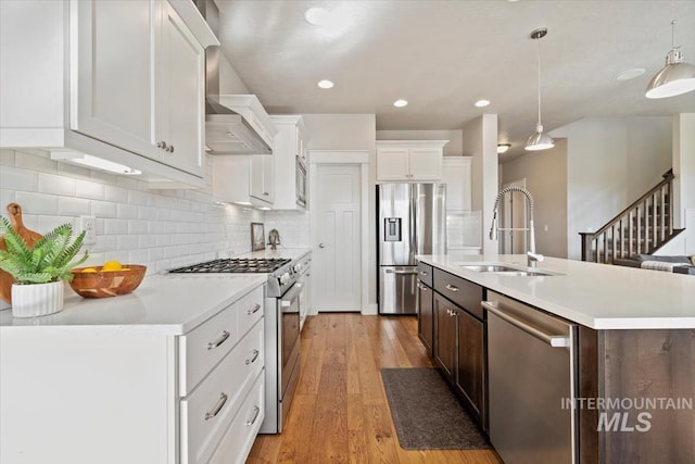 kitchen featuring sink, appliances with stainless steel finishes, an island with sink, white cabinets, and decorative light fixtures