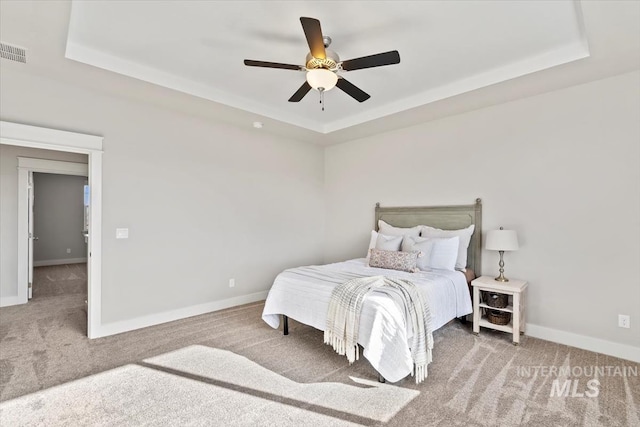 carpeted bedroom with a raised ceiling and ceiling fan