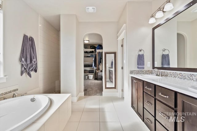 bathroom featuring tile patterned flooring, vanity, backsplash, and tiled tub