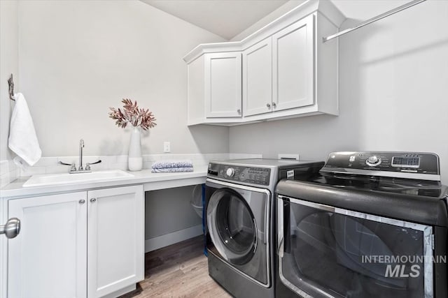 washroom featuring cabinets, washing machine and clothes dryer, sink, and light hardwood / wood-style flooring