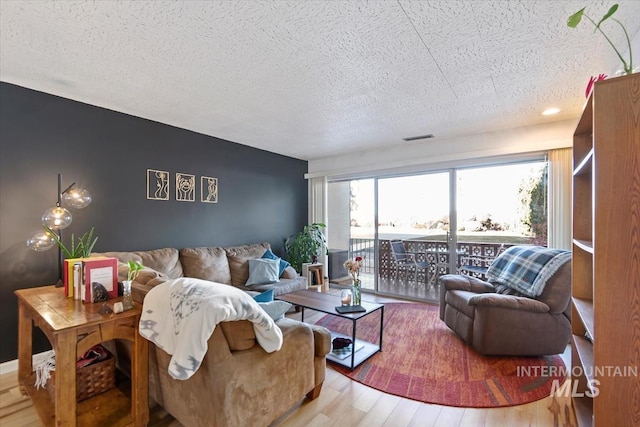 living area featuring a textured ceiling, light wood finished floors, and visible vents