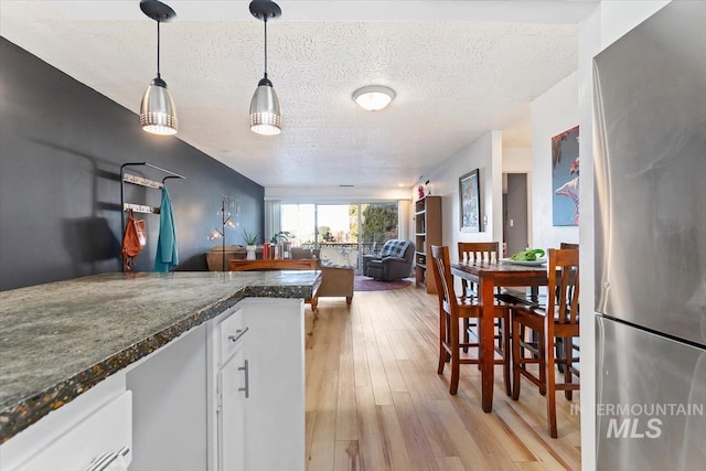 kitchen with a textured ceiling, white cabinets, light wood-type flooring, freestanding refrigerator, and decorative light fixtures