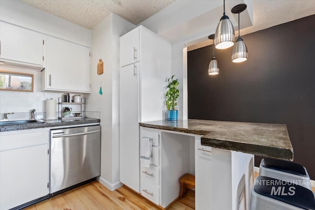 kitchen featuring dark countertops, stainless steel dishwasher, white cabinets, a sink, and light wood-type flooring