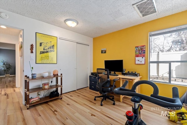 office space featuring light wood finished floors, visible vents, and a textured ceiling