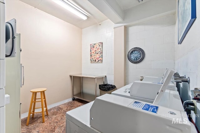 common laundry area with baseboards, concrete block wall, and washer and dryer