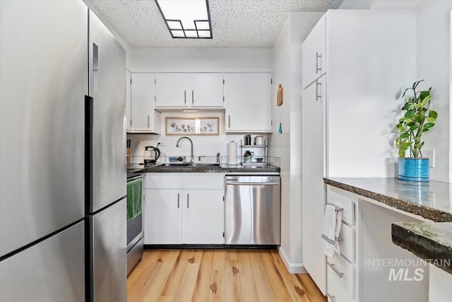 kitchen with appliances with stainless steel finishes, white cabinetry, a sink, and light wood-style flooring