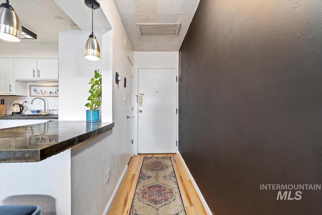 entryway with light wood-type flooring, a sink, visible vents, and baseboards